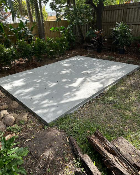 New concrete slab in a backyard garden, with old timber sleepers beside it