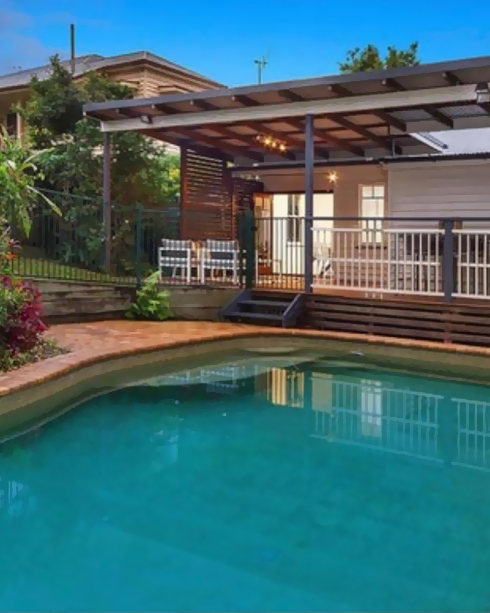 Pool with terracotta paved surrounds in front of a house with a covered deck